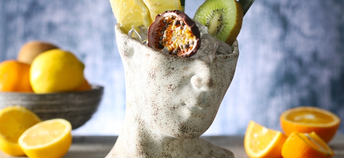 Tiki Mugs

1 Head Tiki Cocktail Cup filled with ice cubes, 2 lemon slices, 1 kiwi slice, 2 straws, 2 pineapple leaves and a Frona Dried Passion Fruit Slice. With a bowl of lemons in the background and orange slices