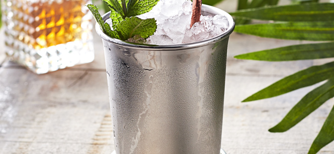 Julep Cup

1 Julep Cup filled with crushed ice, mint leaves and straw, accompanied with a bitter bottle in the background along with leaves